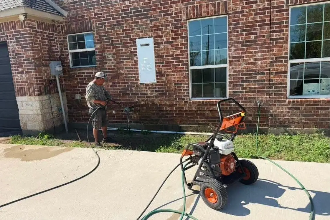 Worker power washing along a brick house with a pressure washer